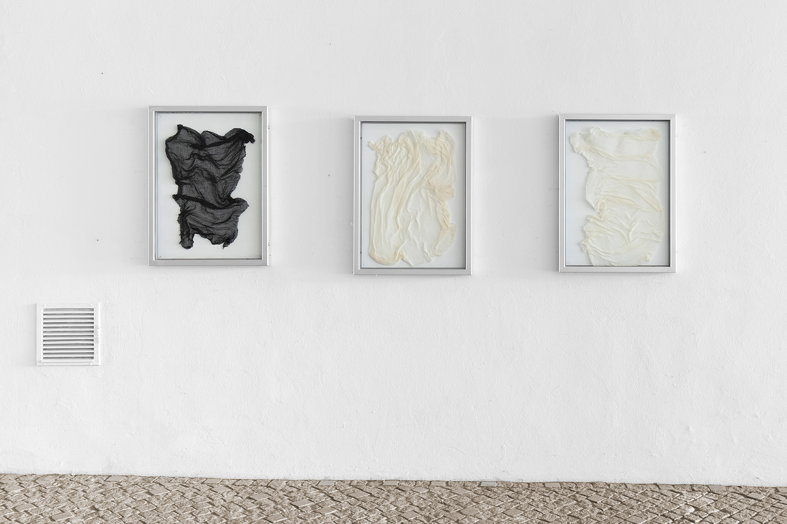 three poster frames on a wall in an outdoor space withe different fabrics inside them